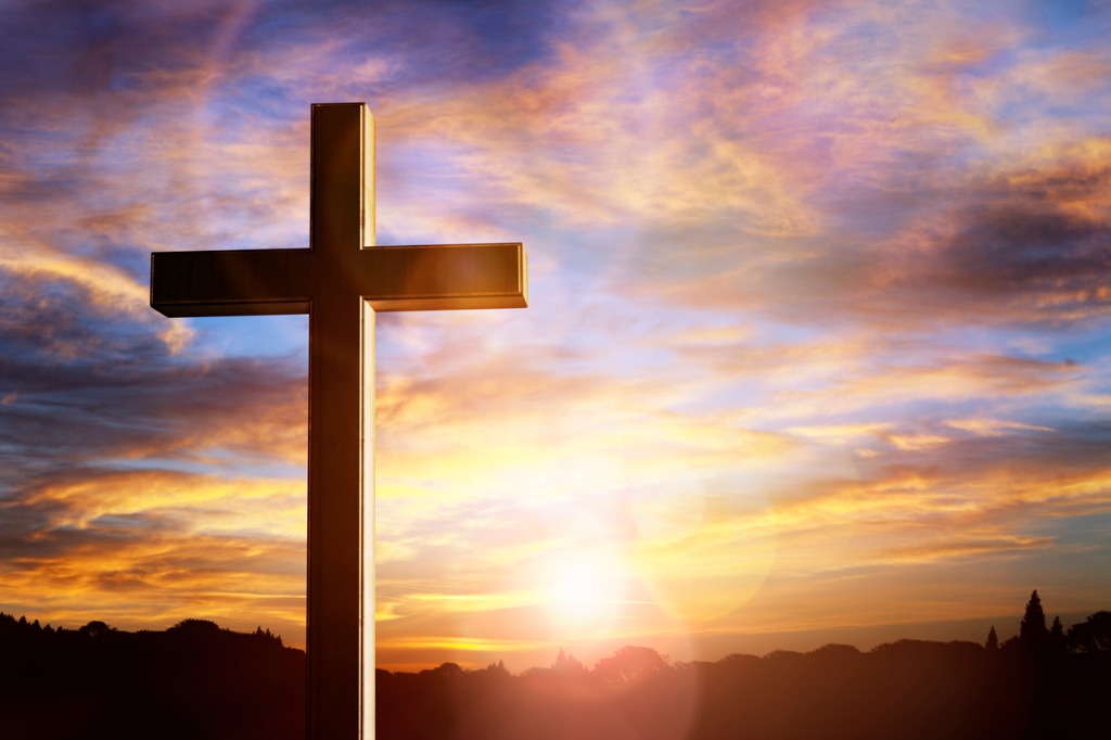 A cross is in front of the sun setting.