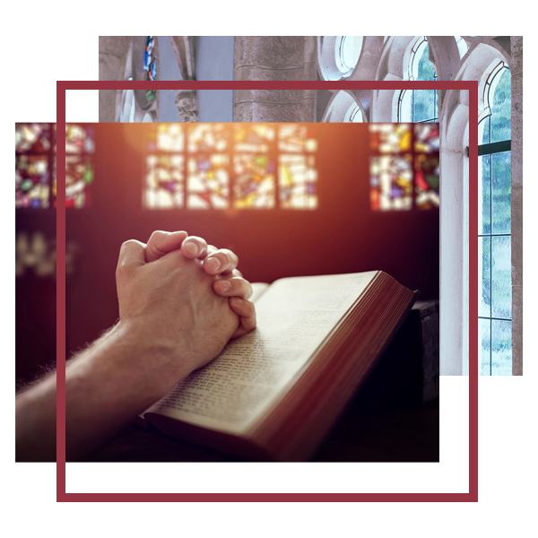 A person is praying on the bible in front of stained glass windows.