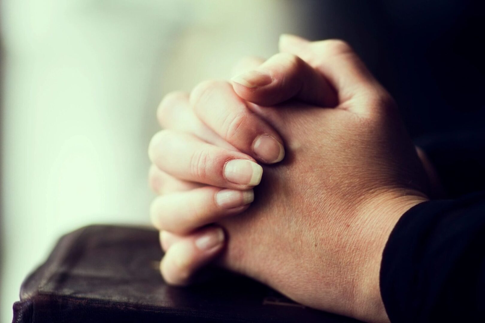 A person 's hands folded in prayer on top of a table.