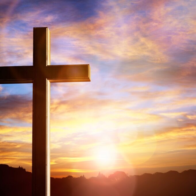 A cross is in front of the sun setting.