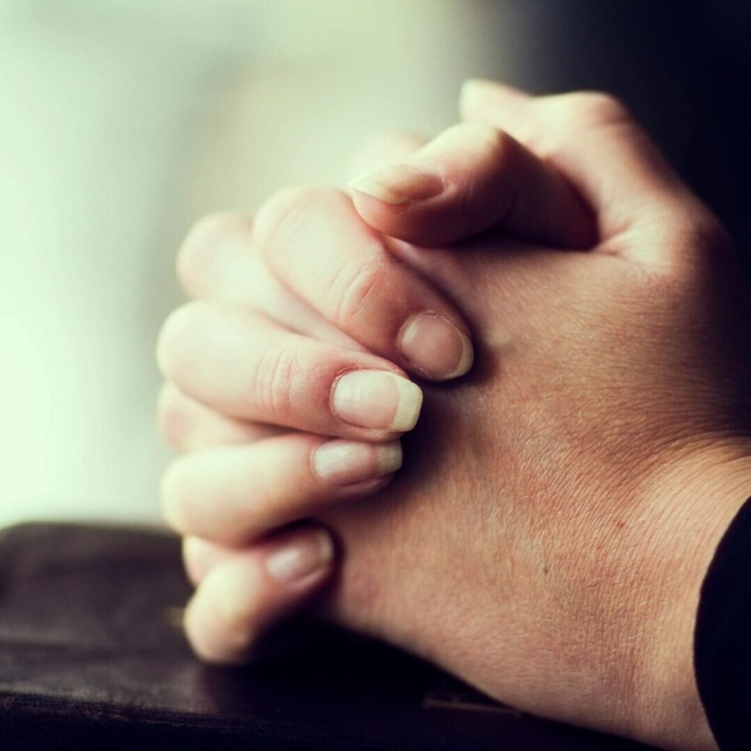 A person 's hands folded in prayer on top of a table.