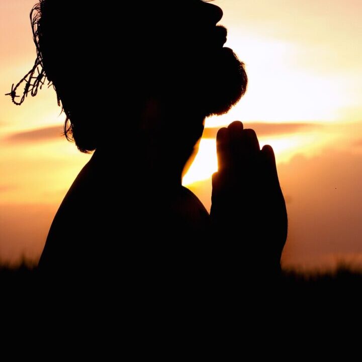 A person is praying in the sunset.